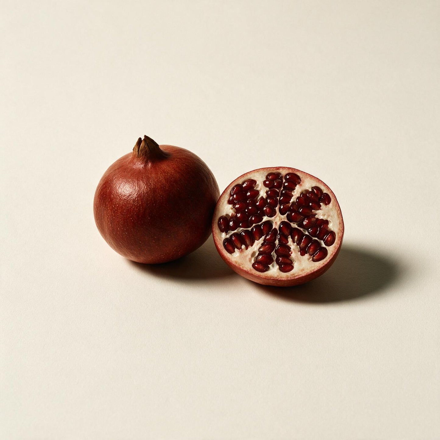Whole and halved pomegranate (Punica granatum) on a seamless off-white background